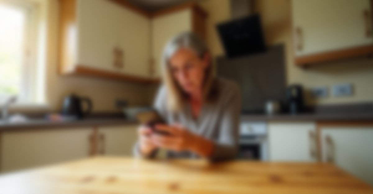 Woman at kitchen table looking concerned at her phone while reading an email