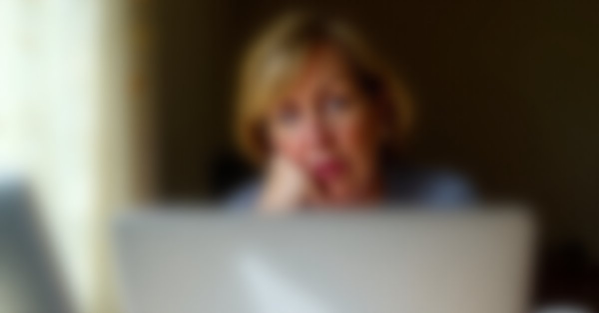 Worried woman at kitchen table with holiday booking printout, looking concerned at her phone