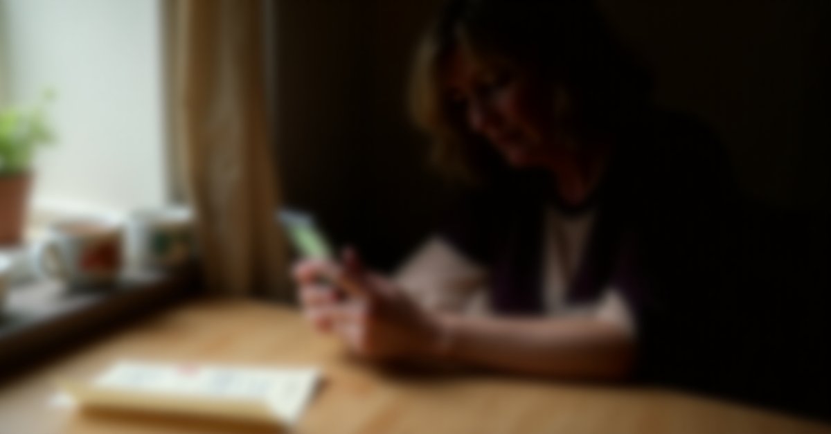 Woman at kitchen table looking worried at her phone, reading what appears to be a suspicious official-looking text message